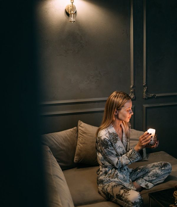 Woman in a calm, focused pose in a dimly lit room with warm ambient light.